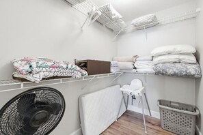 A laundry room with a fan, a radiator, a chair, and storage shelves with folded clothes and a box. - 1 Block to Beach | New Outdoor Living Space (St Augustine)