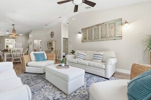 Un salon avec un canapé blanc, un pouf et un tapis à motifs.