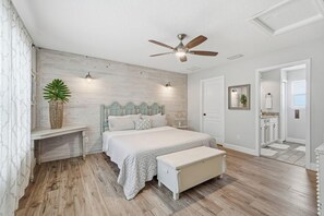 Une chambre à coucher comprenant un lit, un banc, un ventilateur de plafond et une table de chevet.