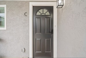 A door with a simple design, a small window above it, and a wall-mounted light fixture to the right.