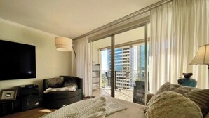 A modern living room with a flat-screen TV, a sofa, a coffee table, and a balcony with a view of high-rise buildings. - Perfect Ocean view 2-bedroom condo that’s centrally located near Ala Moana beach (Honolulu)