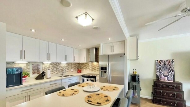 A modern kitchen with white cabinets, a stainless steel refrigerator, and a dining table with placemats. - Perfect Ocean view 2-bedroom condo that’s centrally located near Ala Moana beach (Honolulu)