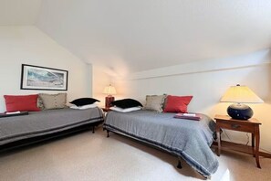 A bedroom with two beds, each with a pillow and a blanket, a bedside table with a lamp, and a framed picture on the wall. - Mountainside Retreat @ Attitash, Ski-In, Ski-Out, Pool, Hiking (Bartlett)
