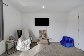 A room with a flat-screen TV mounted on the wall, a blue bean bag chair, a white chair with a textured blanket, and a small table with a statue and a mosaic piece. - Spacious Vegas Retreat • Close to Strip • Sleep 12 (Las Vegas)