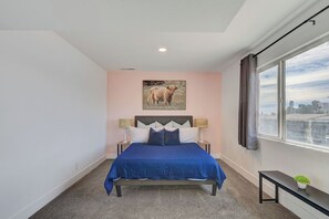 A bedroom with a bed, a nightstand, a lamp, a window with curtains, and a painting on the wall. - Spacious Vegas Retreat • Close to Strip • Sleep 12 (Las Vegas)