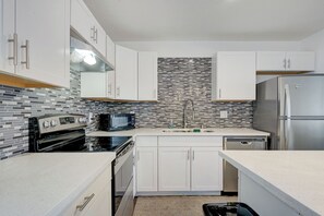 A modern kitchen with white cabinets, a stainless steel refrigerator, a microwave, and a tiled backsplash. - Spacious Vegas Retreat • Close to Strip • Sleep 12 (Las Vegas)