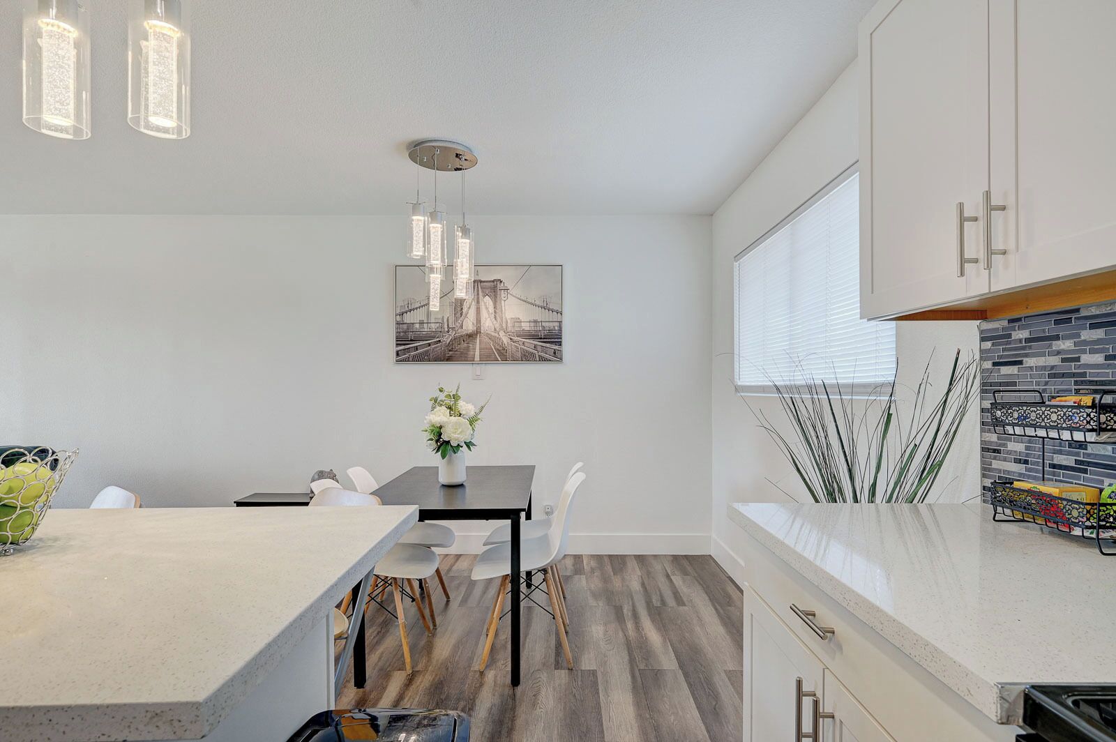 A modern kitchen with a central island, pendant lighting, and a dining area with a table and chairs.