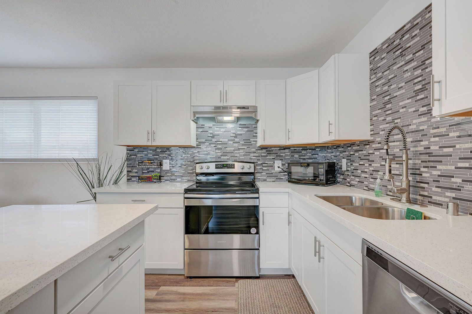 A modern kitchen with white cabinets, a stainless steel oven, a microwave, and a tiled backsplash.