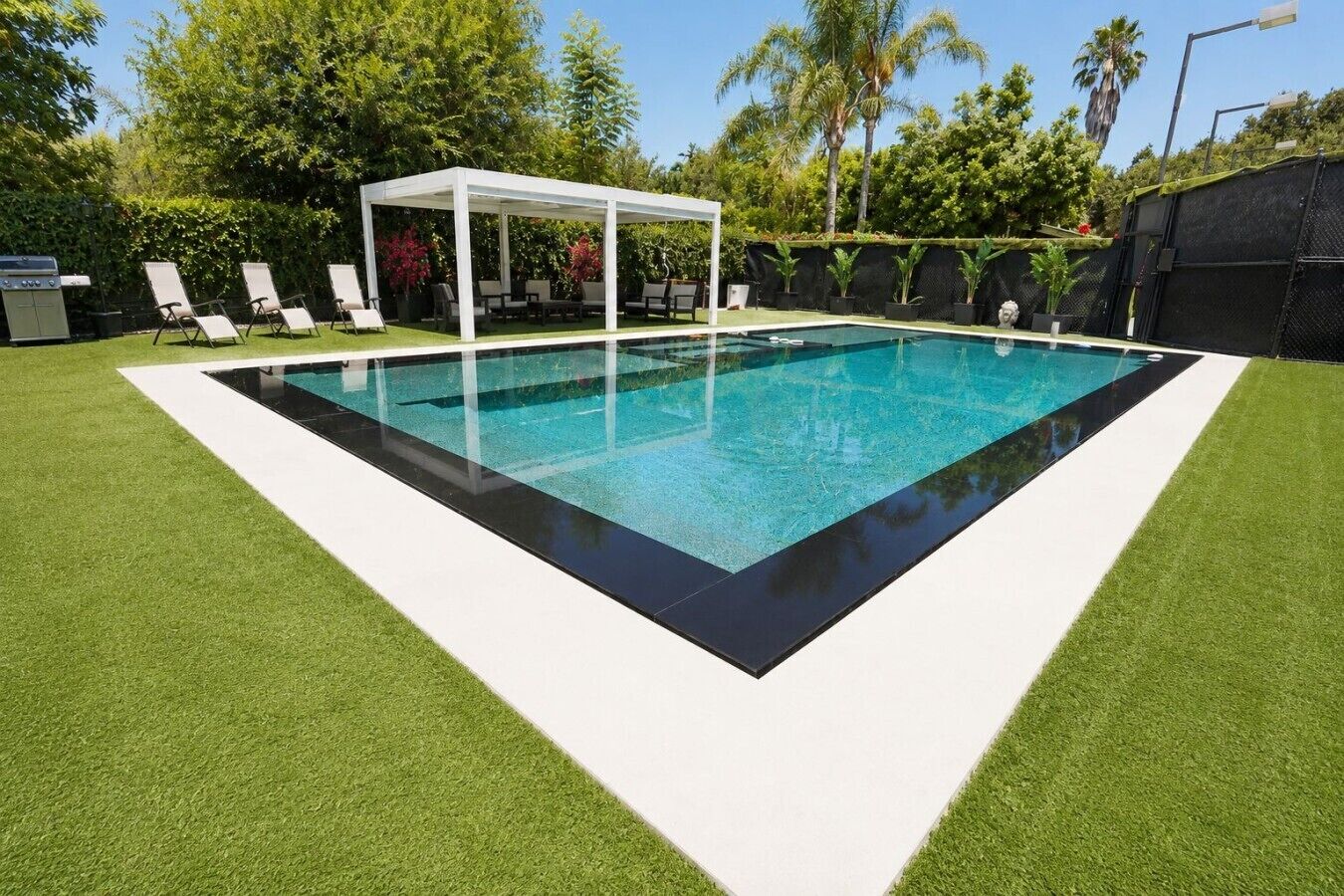 Une piscine rectangulaire dotée d’une plage blanche et d’un espace salon abrité.