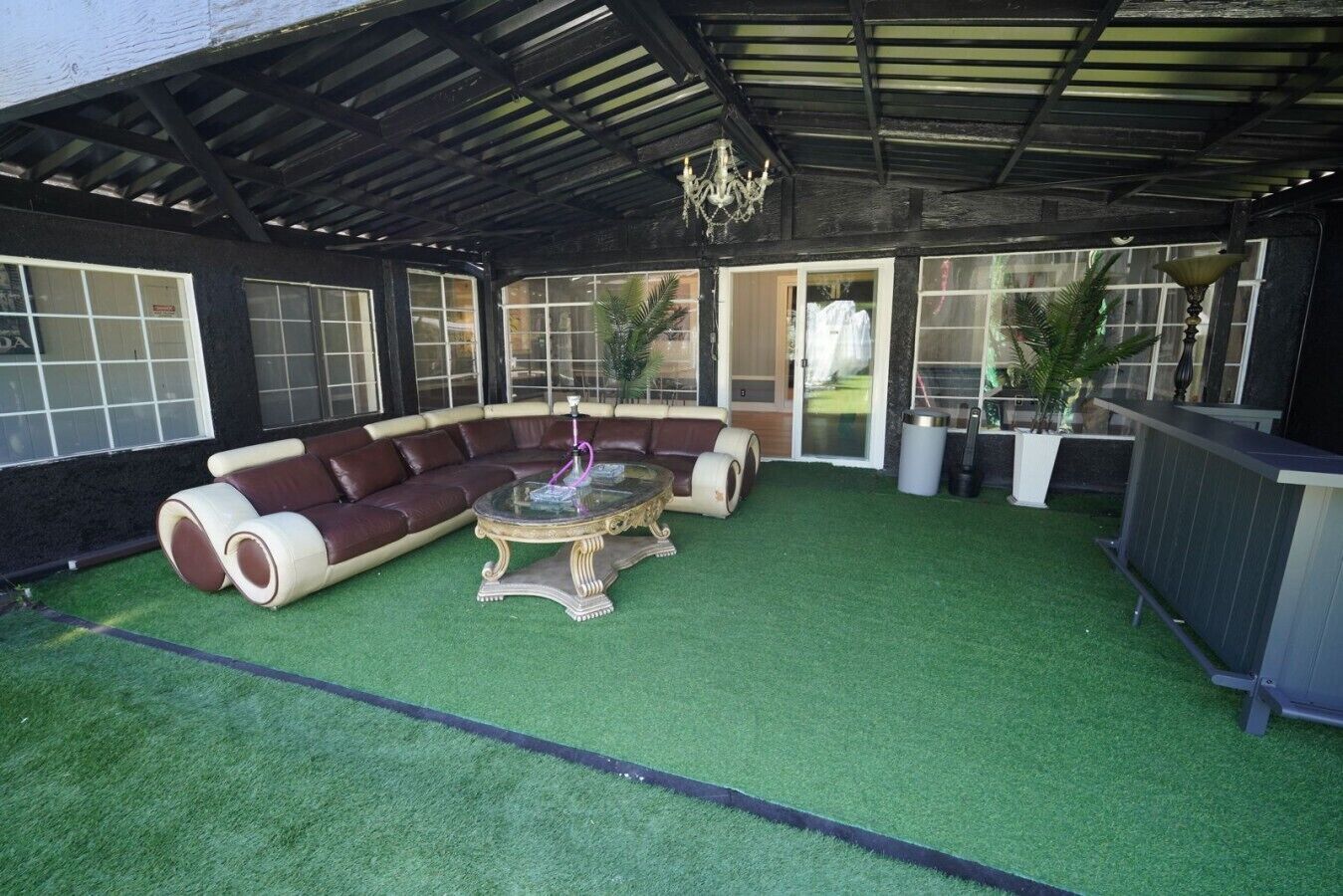 Ein überdachter Außenbereich mit Ecksofa und rundem Tisch, umgeben von Kübelpflanzen und einer Pergola.