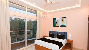 A bedroom with a bed, a ceiling fan, a nightstand, and a large window. - Townhouse Tender Village Seven Seas (Ranchi)