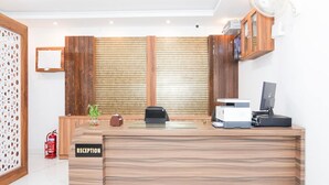 A reception desk with a wooden finish, a fire extinguisher, a potted plant, and a wall-mounted fan. - Townhouse Tender Village Seven Seas (Ranchi)