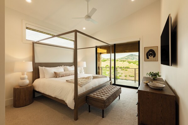 A four-poster bed with a view of a desert landscape through a sliding glass door.