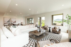 Un salon moderne avec un canapé blanc, une table basse et une vue sur un paysage désertique, visible à travers une grande fenêtre.
