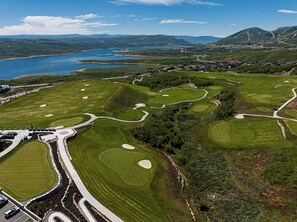 An aerial view of a golf course with multiple holes, a parking area, and a body of water in the background.
