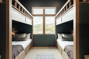 A room with two bunk beds, a window with a view of a landscape, and a patterned rug on the floor.