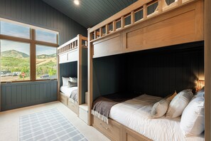 A bedroom with a bunk bed, a large window with a view of a hilly landscape, and a wooden headboard.