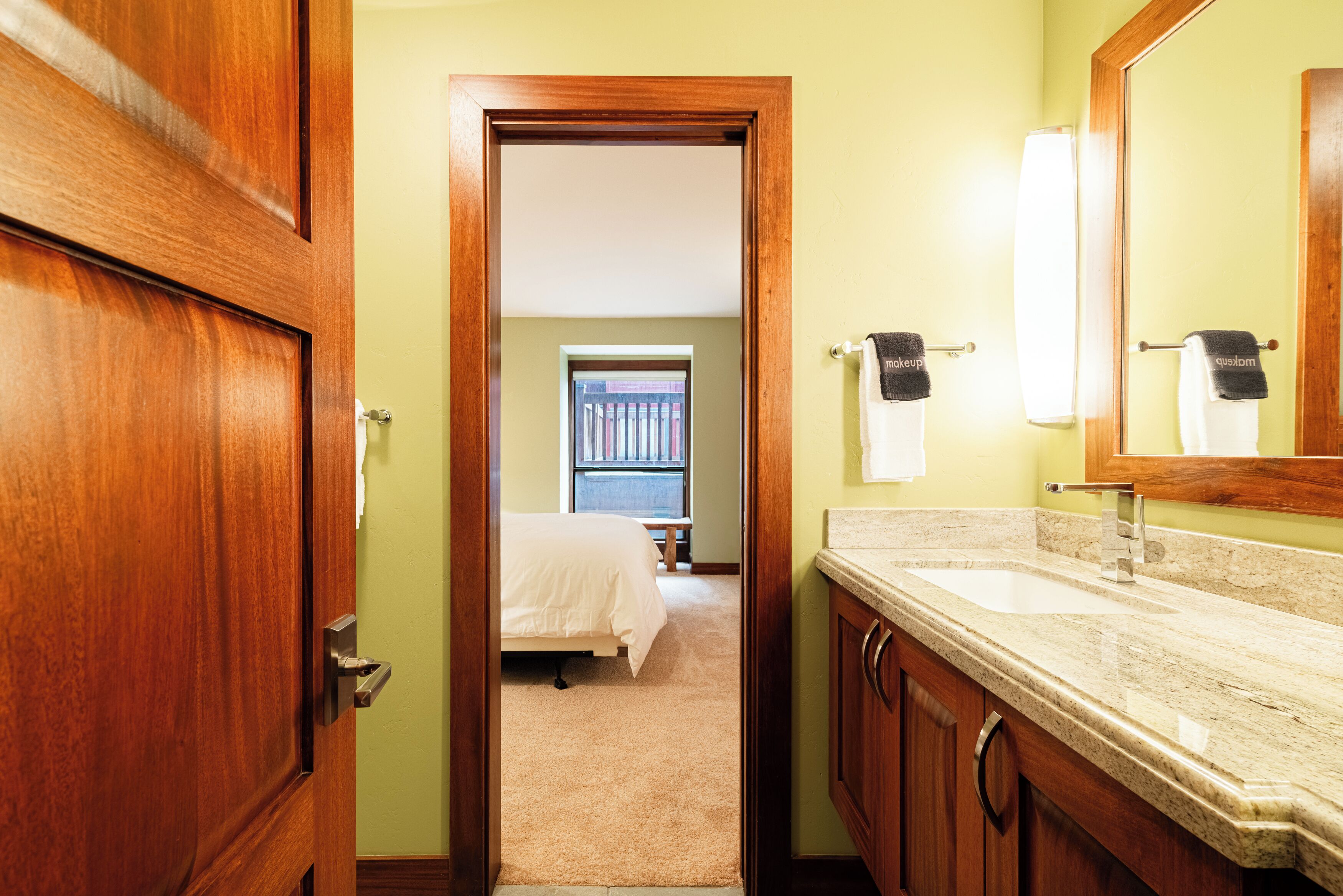 A hotel bathroom with a wooden door, a sink, and a mirror.