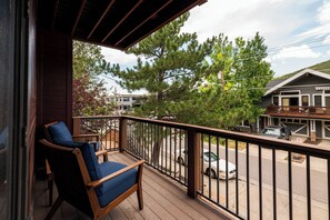 Eine Holzterrasse mit Stuhl und Geländer, mit Blick auf eine Straße mit Autos und Häusern.