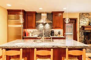 Eine Küche mit Granit Arbeitsplatten, Holzschränken, einem Edelstahl-Kühlschrank und Pendelleuchten.