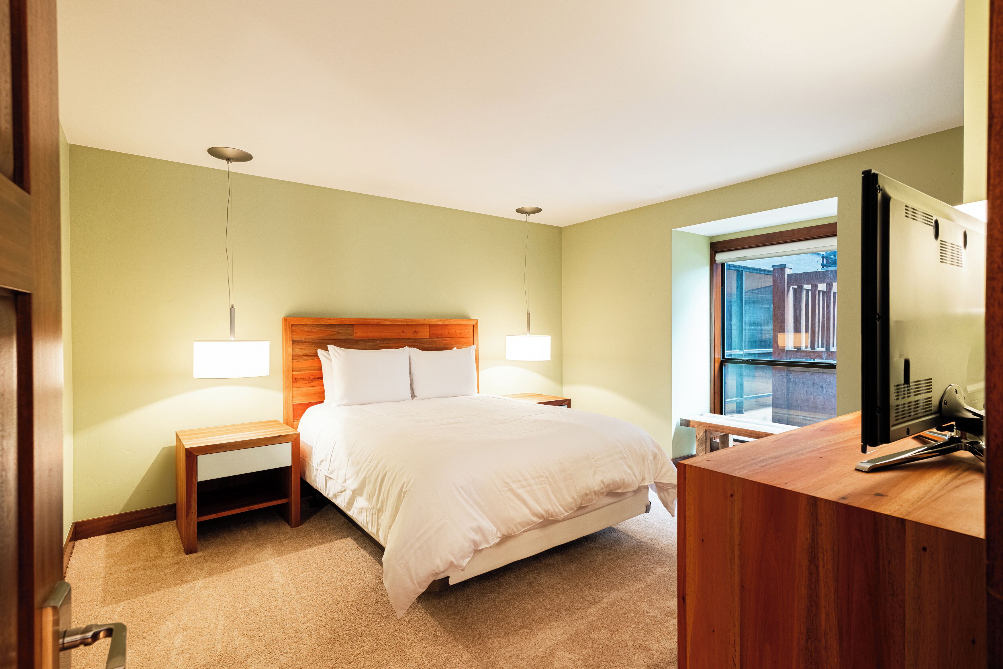Ein Hotelzimmer mit Bett, Nachttischen, einem Schreibtisch mit Computer und einem Fenster mit Blick auf einen Balkon.