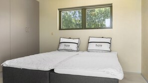 Ein Doppelbett mit zwei Kissen, ein Fenster mit Blick auf Bäume und ein Kleiderschrank.
