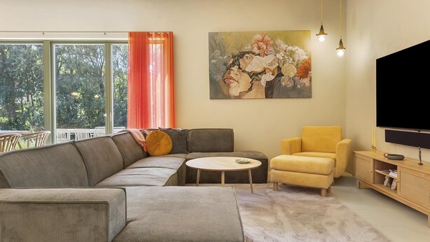 En moderne stue med en hjørnesofa, en gul lænestol, et rundt sofabord og et fladskærms-tv.