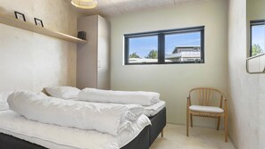 A bedroom with a bed, a chair, a window, and a shelf with books. - VillaVilla 988 - Hostrup Strand, Limfjorden (Spøttrup)