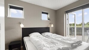 A double bed with a black headboard, two bedside lamps, and a view of the outdoors through a sliding glass door. - VillaVilla 974 - Hvide Sande, Vestjylland (Hvide Sande)