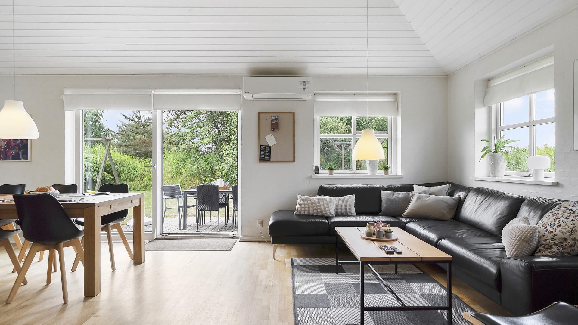 Un salon moderne avec un canapé en cuir noir, une table basse en bois et un coin repas comprenant une table et des chaises.