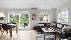 A modern living room with a black leather sofa, a wooden coffee table, and a dining area with a table and chairs. - VillaVilla 974 - Hvide Sande, Vestjylland (Hvide Sande)