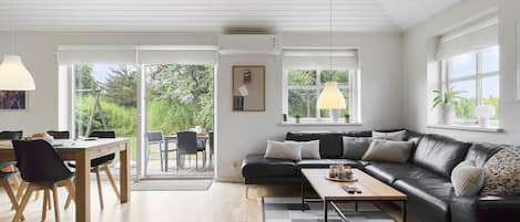 Una sala de estar moderna con un sofá de cuero negro, una mesa de centro de madera y un comedor con mesa y sillas.