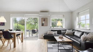 A modern living room with a black leather sofa, a wooden coffee table, and a dining area with a table and chairs. - VillaVilla 974 - Hvide Sande, Vestjylland (Hvide Sande)