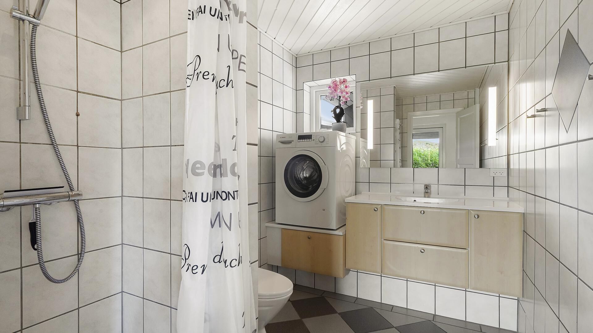 Une salle de bain moderne équipée d’un lave-linge, de toilettes et d’un rideau de douche orné de motifs textuels.