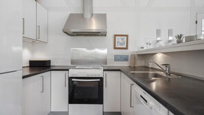 A modern kitchen with white cabinetry, a stainless steel range hood, a built-in oven, and a dishwasher. - VillaVilla 974 - Hvide Sande, Vestjylland (Hvide Sande)