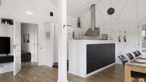 A modern kitchen with a central island, a dining area with a wooden table, and a television in a corner. - VillaVilla 974 - Hvide Sande, Vestjylland (Hvide Sande)