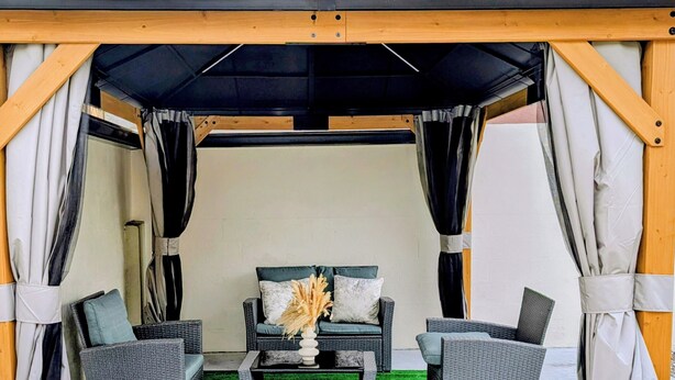 A covered outdoor seating area with a sofa and two armchairs, a coffee table, and a decorative vase. - Delightful 3-bedroom house with AC in charming Cunupia (Cunupia)