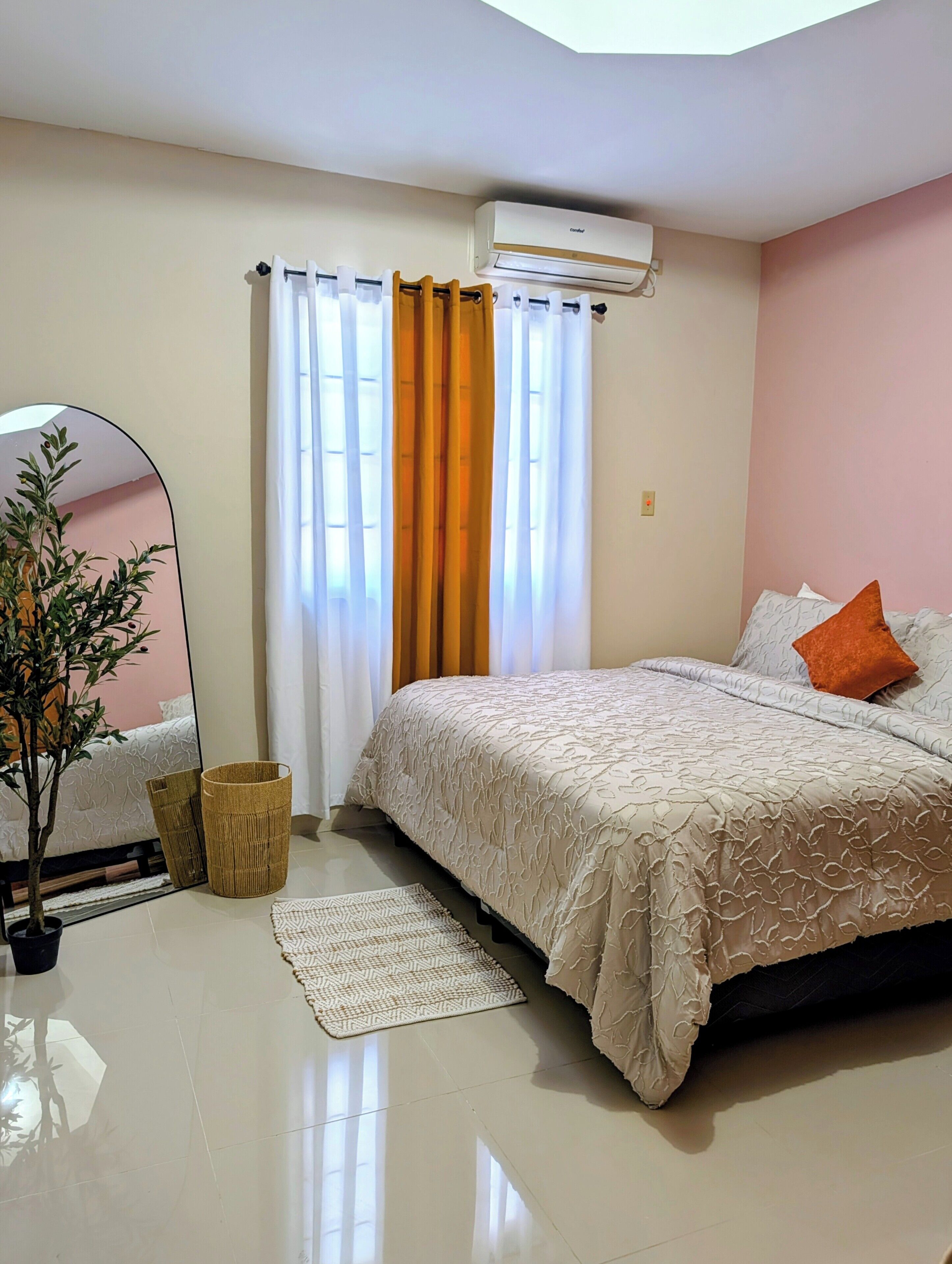Une chambre à coucher avec un lit, un miroir, une plante en pot, un panier et un tapis.