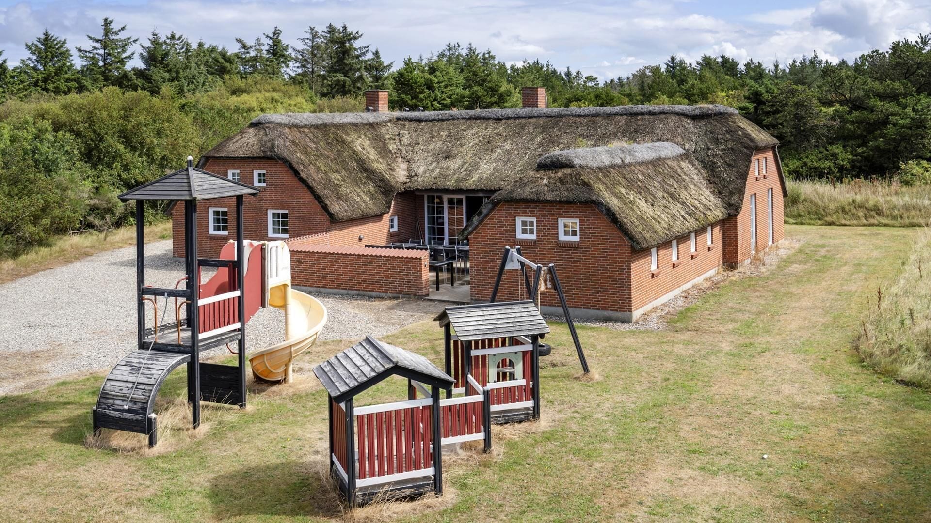 A rustic building with a thatched roof, a play area with a slide, and a small wooden structure.