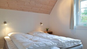 Ein Schlafzimmer mit Holzbalkendecke, zwei Nachttischlampen, einem Fenster mit Blick auf Grünflächen und einem kleinen Nachttisch mit Pflanze.