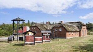 Ein traditionelles Haus mit Strohdach und Spielbereich, inklusive Rutsche und Klettergerüst.