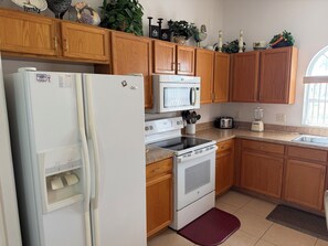 Una cocina con armarios de madera, un refrigerador blanco, un microondas, un horno, un tostador y un fregadero.