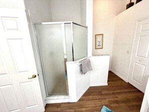 Una habitación con ducha envuelta en vidrio, paredes blancas y suelo de madera.