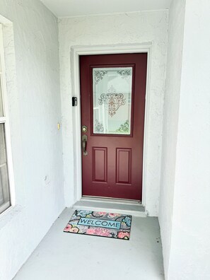 A red door with decorative glass panels and a welcome mat at the entrance. - Magic Stay Kissimmee, Spacious 4-bedroom house with pool, fit up to 8 guests (Kissimmee)
