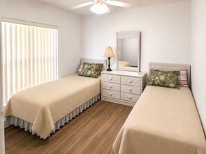 Quarto com duas camas de solteiro, cômoda, espelho e ventilador de teto.