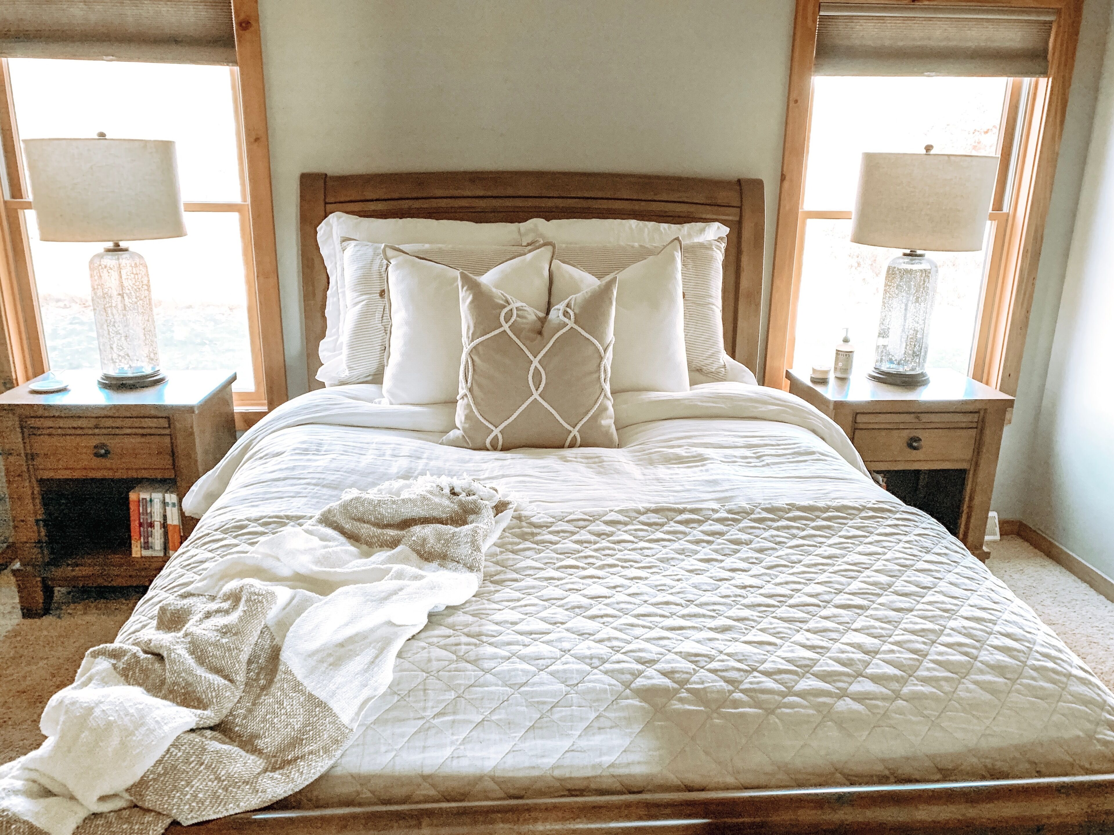 A neatly made bed with a quilted cover, two bedside lamps, and a bedside table with a lamp and books.