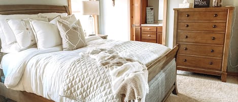 A bedroom with a wooden bed, a nightstand, a dresser, and a mirror.