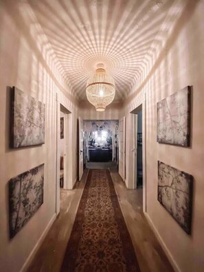 A hallway with a patterned carpet, a chandelier, and framed artwork on the walls. - White Bohemian,2 houses, 9000 sq ft Games, Hot Tub Events - sleeps 34 (Atlanta)