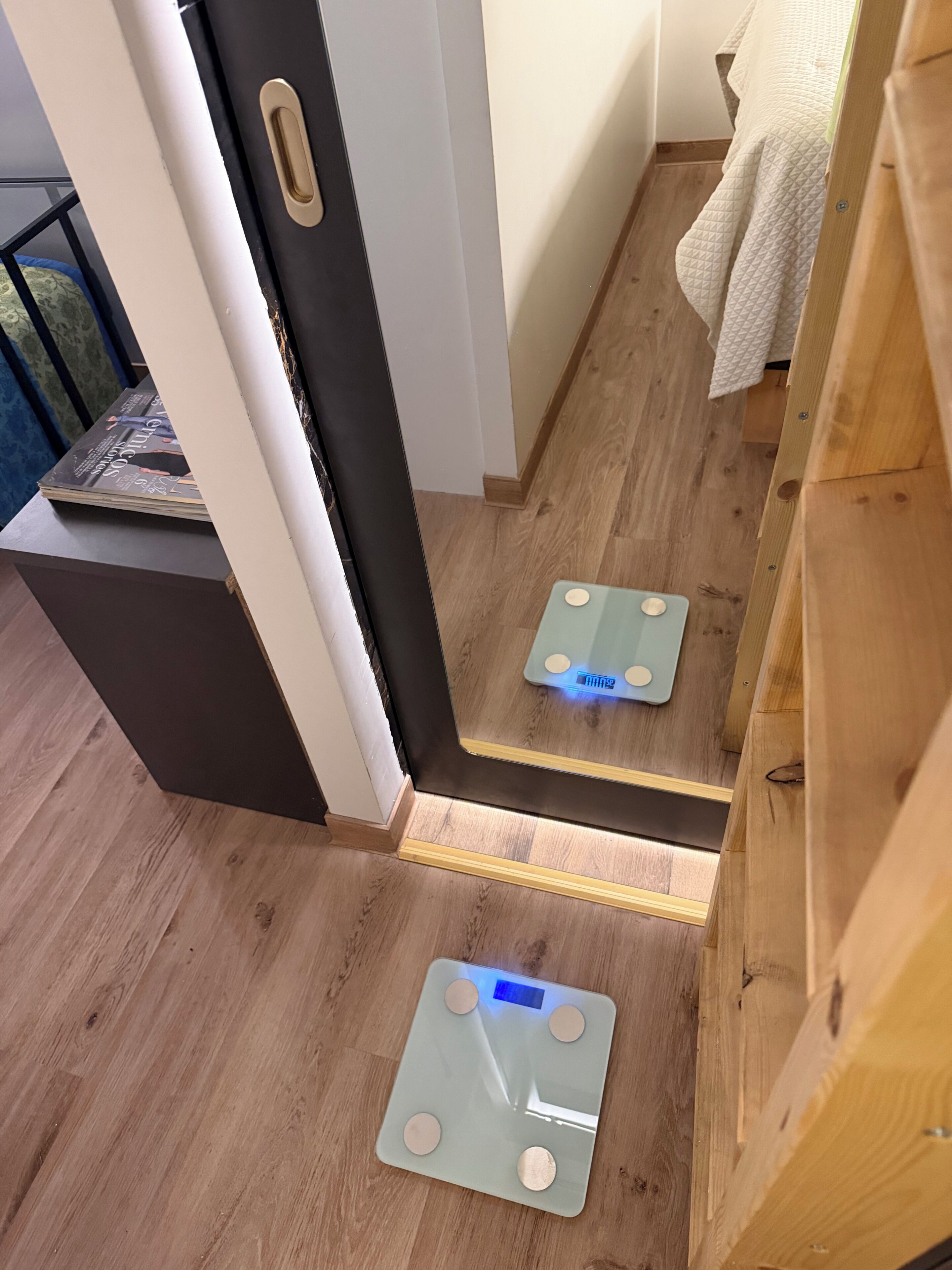 Une salle de bain avec un plancher en bois, une serviette blanche accrochée au mur et une balance posée sur le sol.