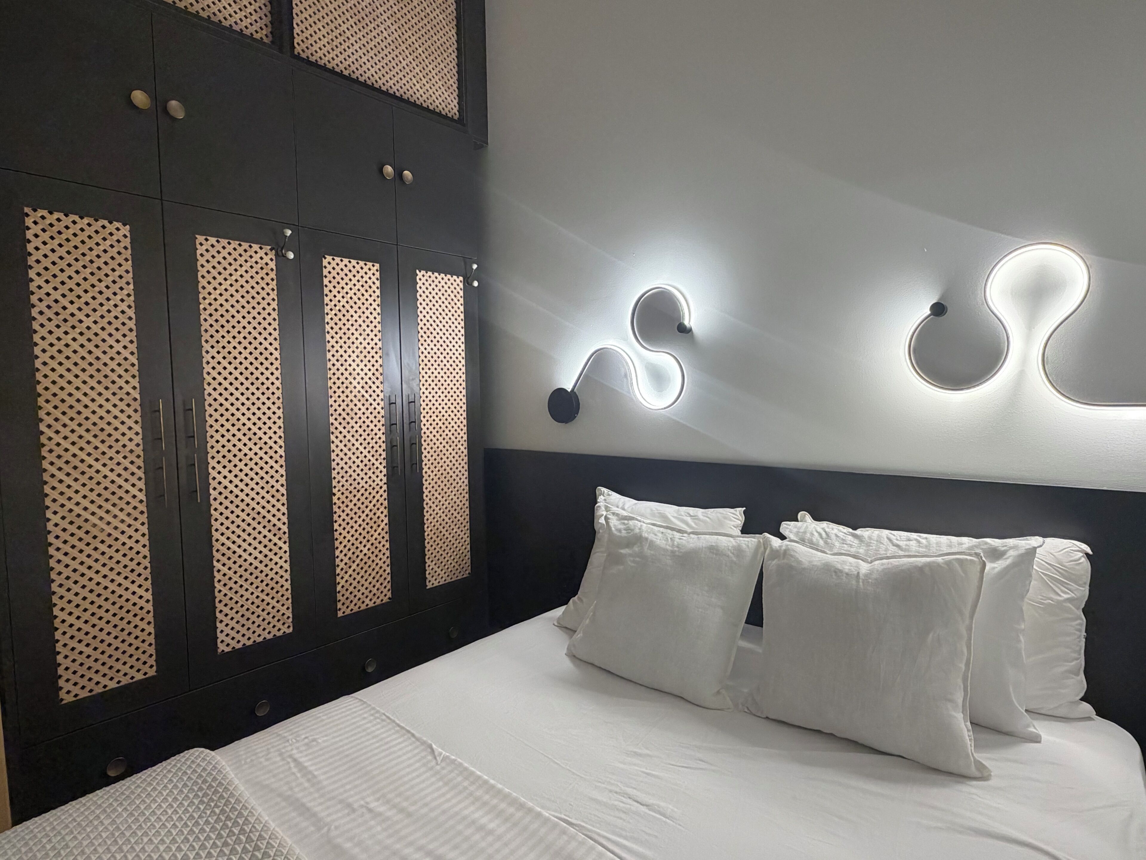 A bedroom with a bed, white pillows, a dark headboard, and a wardrobe with patterned doors.